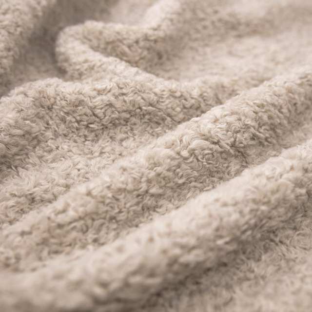 Close-up of warm oatmeal fleece fabric with dense curly pile and softly shaded folds