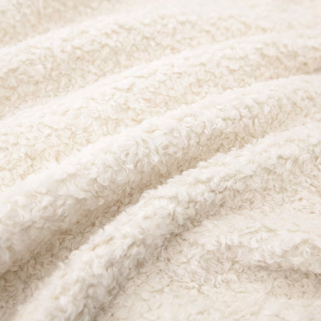 Close-up of ivory fabric with dense curled pile and softly raised folds