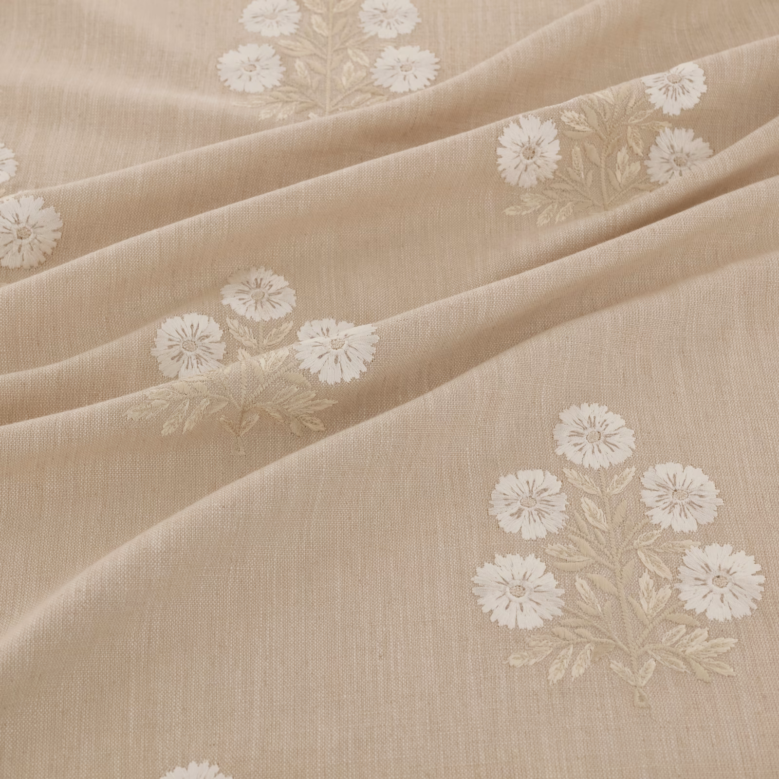 Warm beige woven fabric with ivory floral sprays arranged across softly draped folds