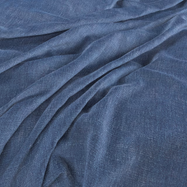 Close-up of muted denim-blue woven fabric gathered into softly shadowed folds