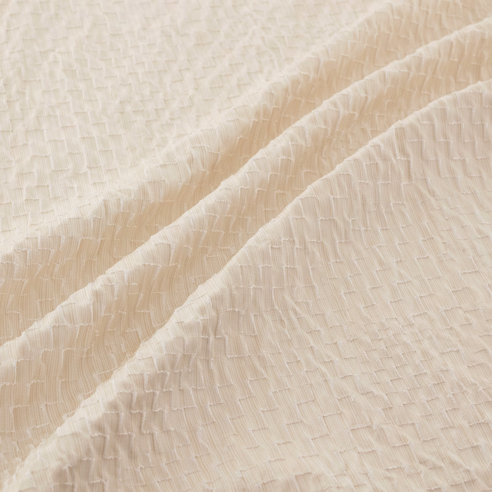 Warm ivory textured fabric with fine raised crinkles falling in soft diagonal folds