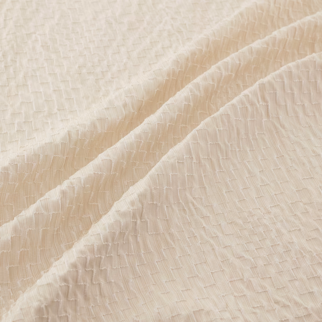 Warm ivory textured fabric with fine raised crinkles falling in soft diagonal folds