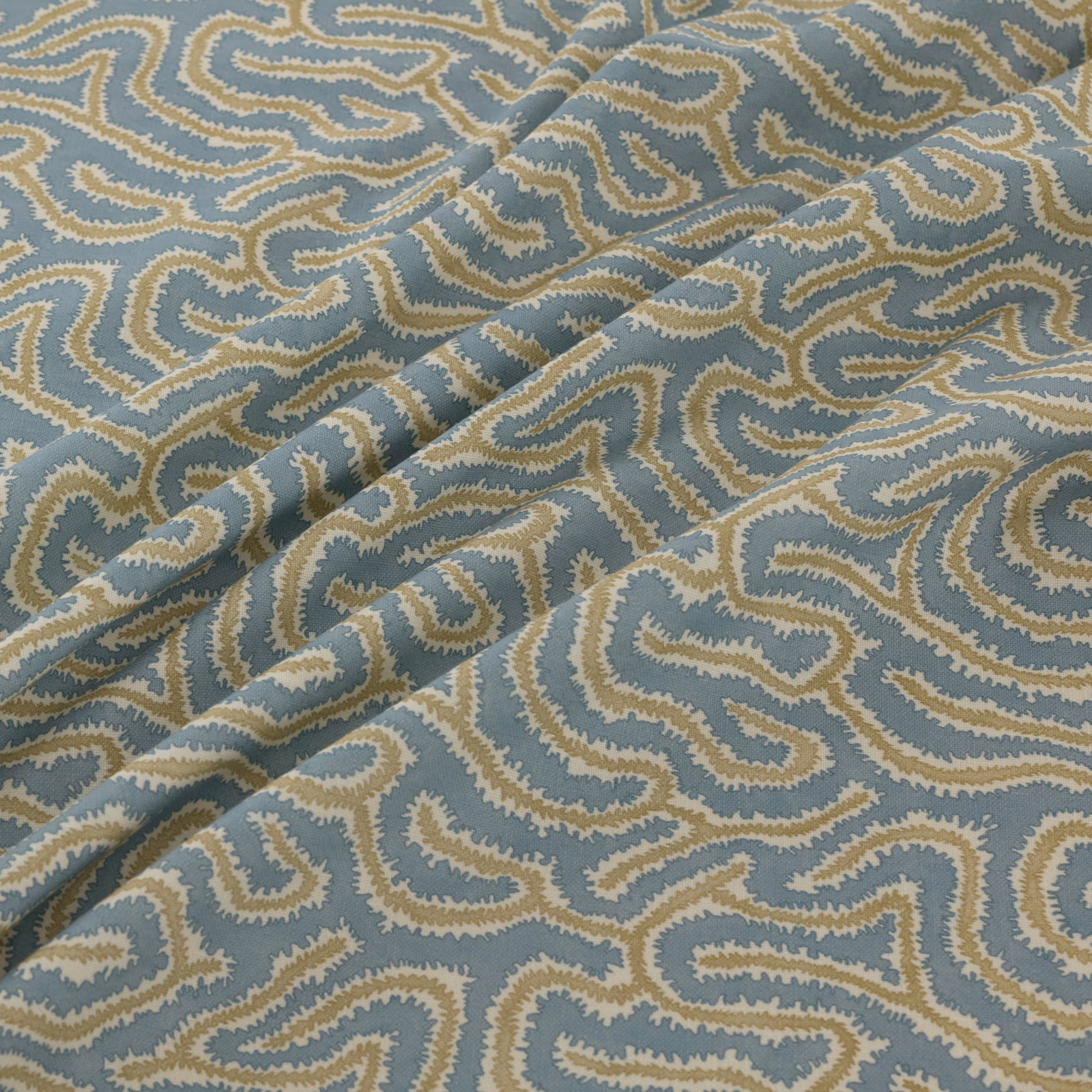 Blue-grey woven fabric with sandy cream meanders and a folded diagonal drape