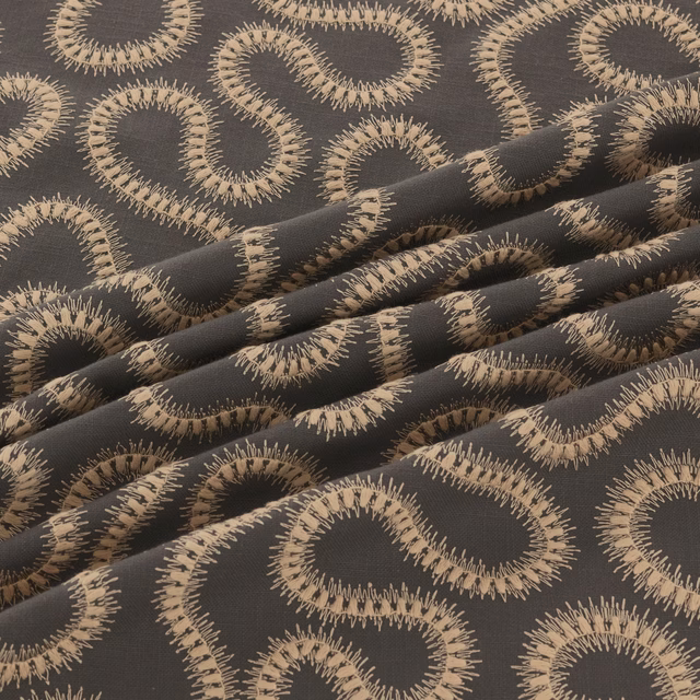 Charcoal woven fabric with large taupe looping motifs and fringed textured edges