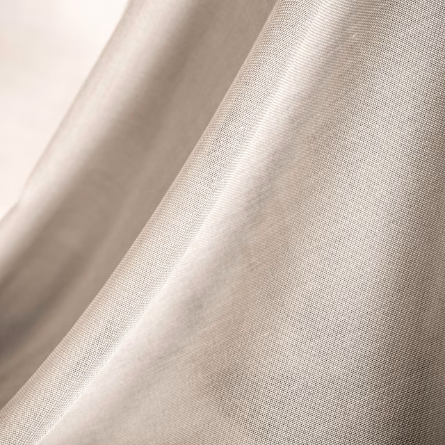 Warm ecru plain woven fabric forming soft folds with fine visible textile grain