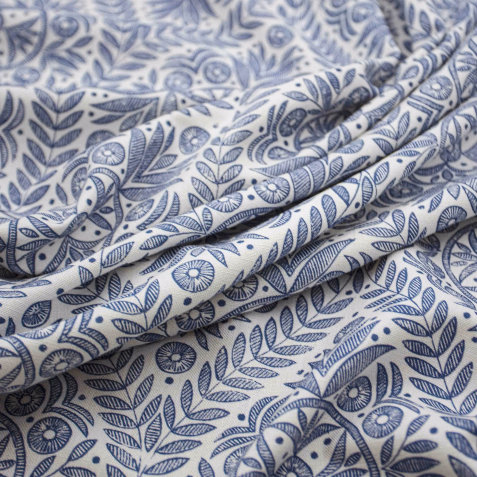 Warm cream fabric with blue botanical sprigs, flowers and softly folded texture