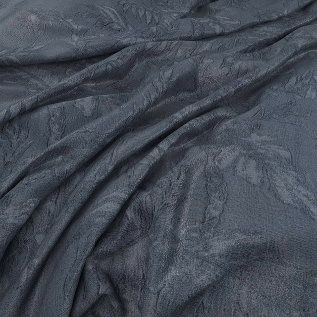 Deep denim blue-grey fabric with tonal leafy motifs and softly textured draped folds