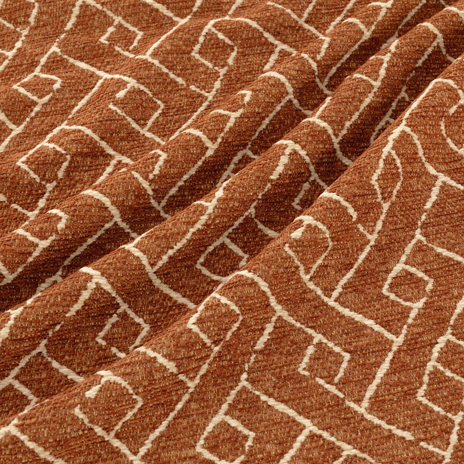 Rust-brown woven textile with cream maze-like geometric lines and tactile texture