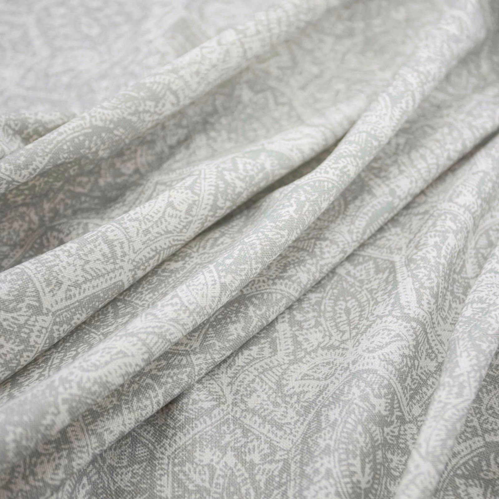 Pale duckegg blue-green fabric with white paisley motifs in soft folded close-up