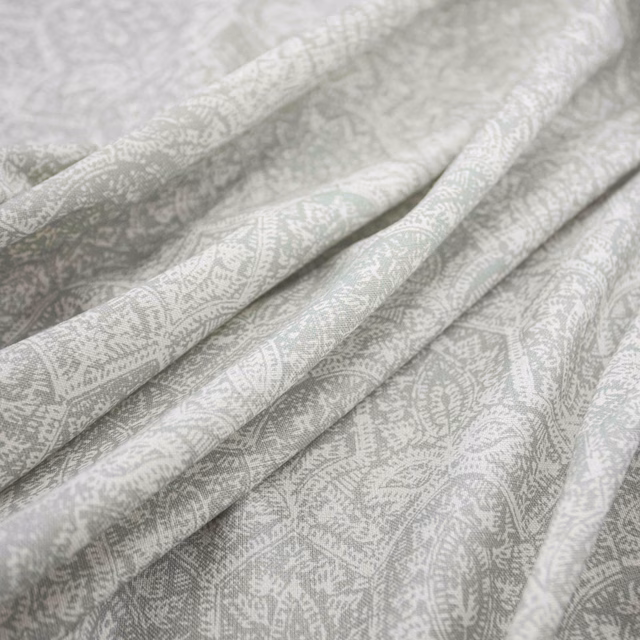 Pale duckegg blue-green fabric with white paisley motifs in soft folded close-up