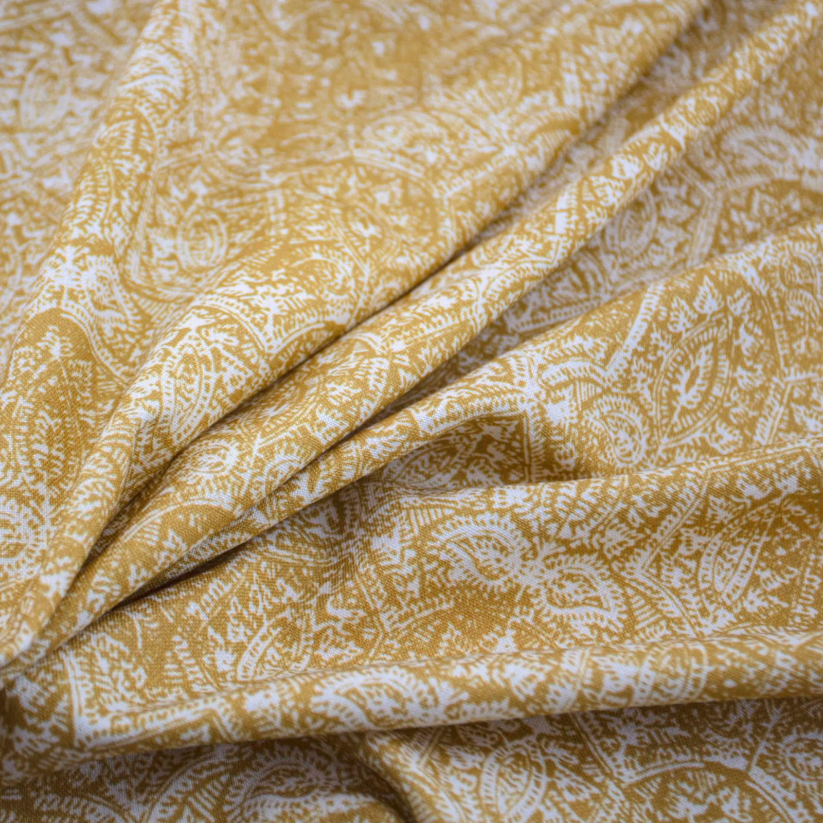 Saffron-gold fabric with pale paisley and leafy motifs folded into soft layered drapes
