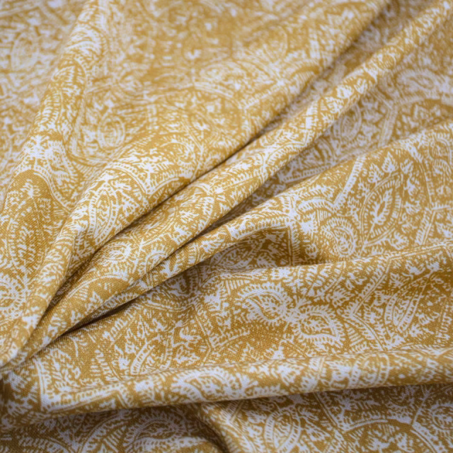 Saffron-gold fabric with pale paisley and leafy motifs folded into soft layered drapes