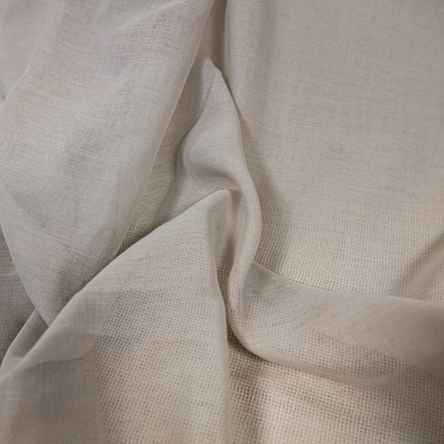 Warm ecru open-weave fabric draped in soft folds with a fine mesh texture