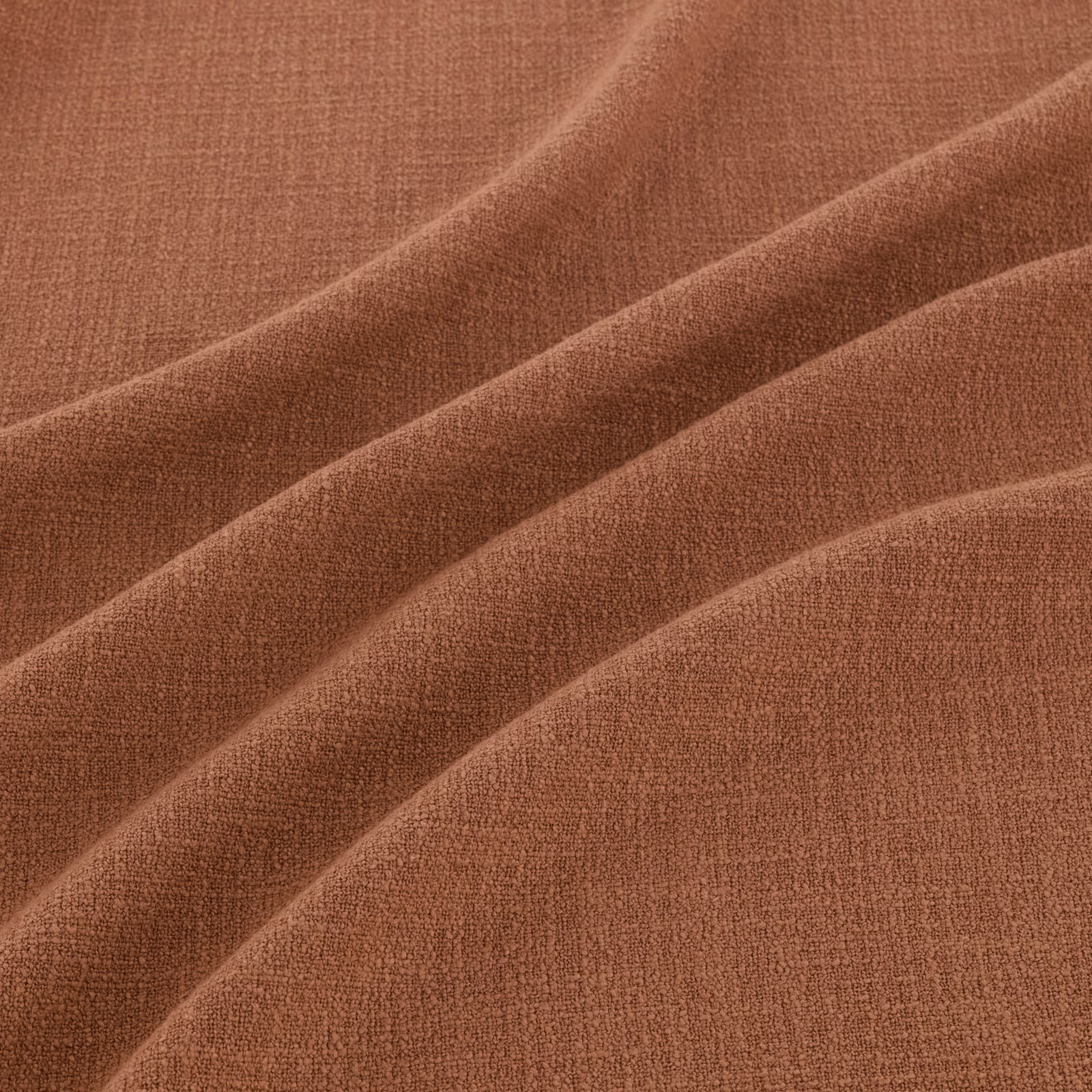 Warm henna terracotta fabric with fine woven texture folded into broad diagonal ridges