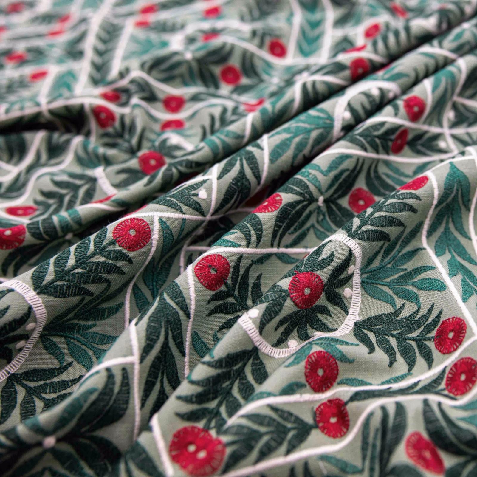 Cream botanical fabric with deep green leaves and berry-red flowers in folded detail