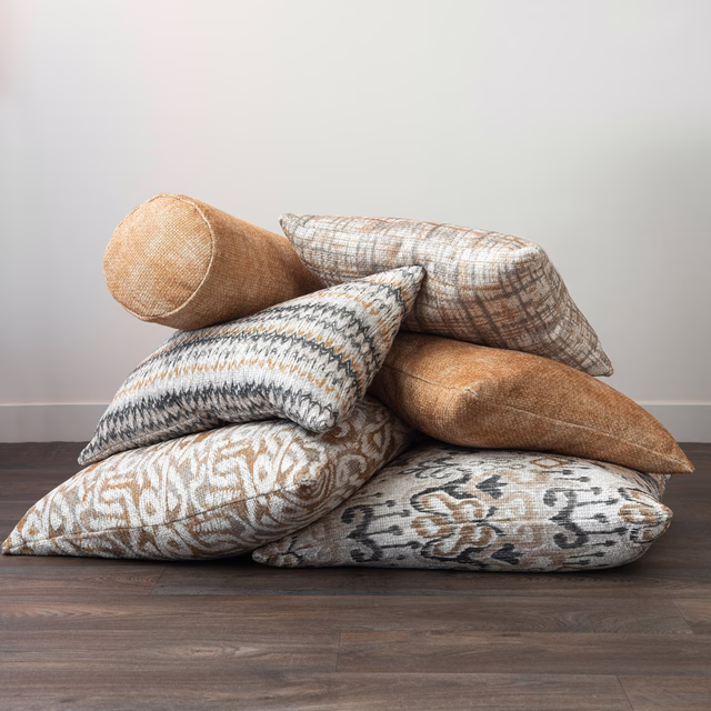 Warm gold woven cushion with fine crosshatched texture among patterned pillows