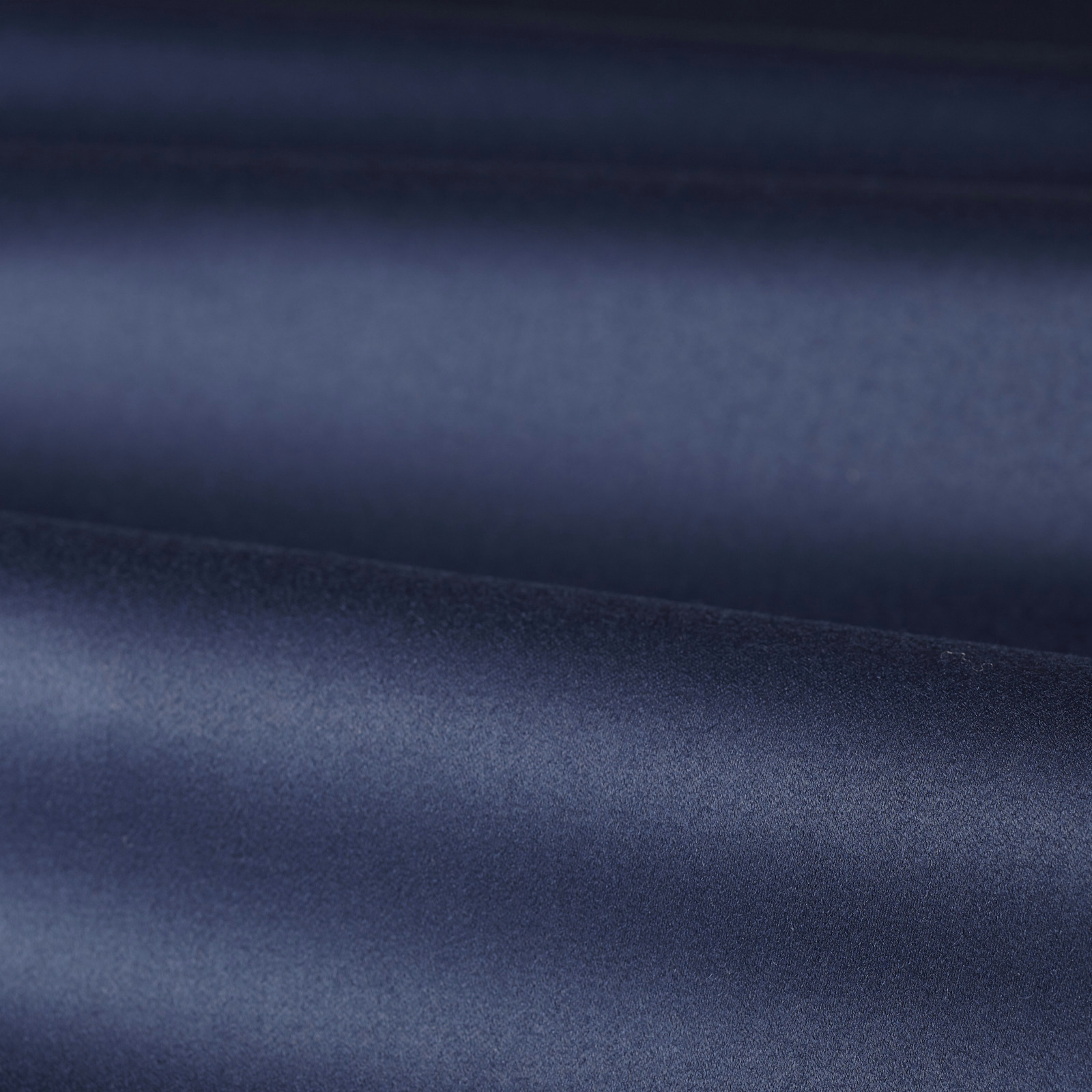 Folded deep indigo blue satin fabric showing smooth sheen and shadowed tonal bands