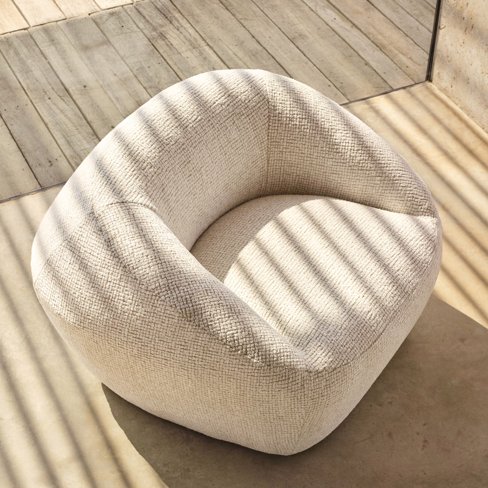 Pale ivory crosshatched upholstery covering a rounded chair in striped sunlight