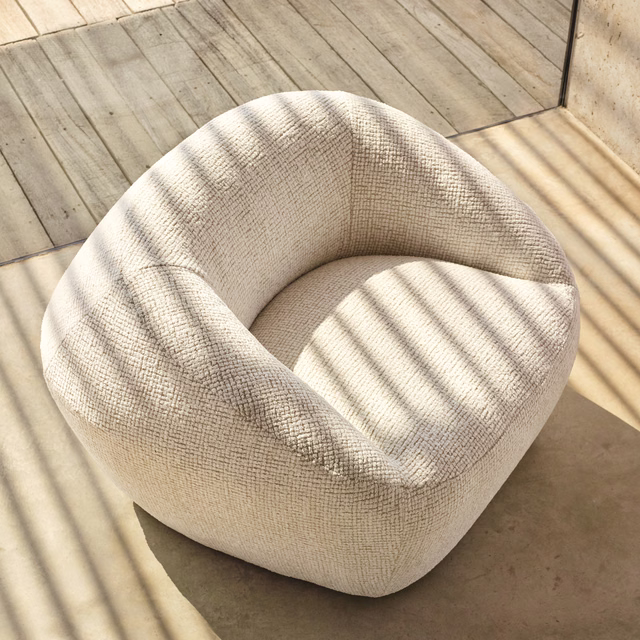 Pale ivory crosshatched upholstery covering a rounded chair in striped sunlight