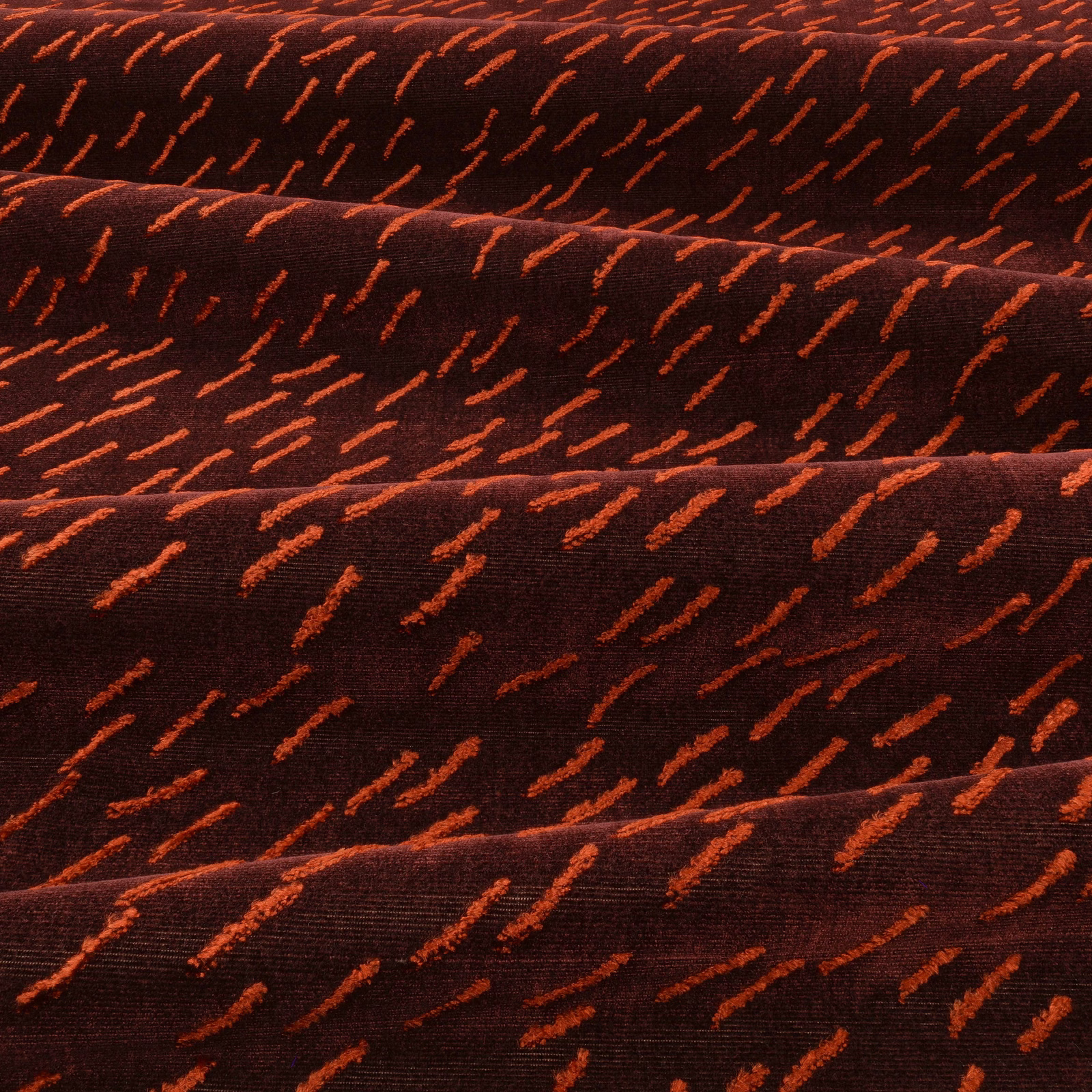 Deep eggplant textile with scattered rust-orange dashes and subtle folded surface texture