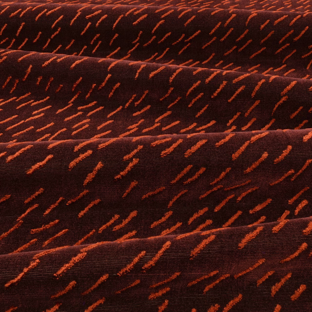 Deep eggplant textile with scattered rust-orange dashes and subtle folded surface texture