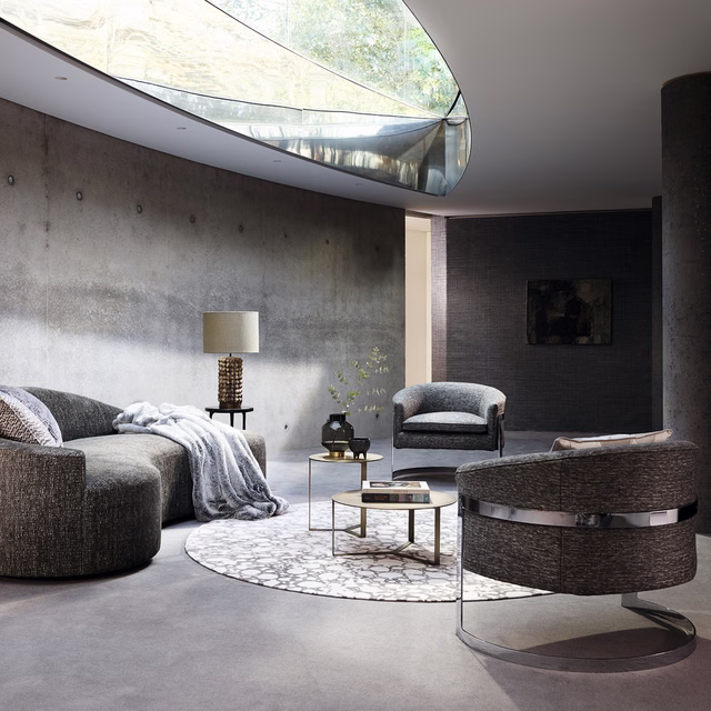 Cool mineral-grey textured upholstery on curved sofa and barrel chair in soft light