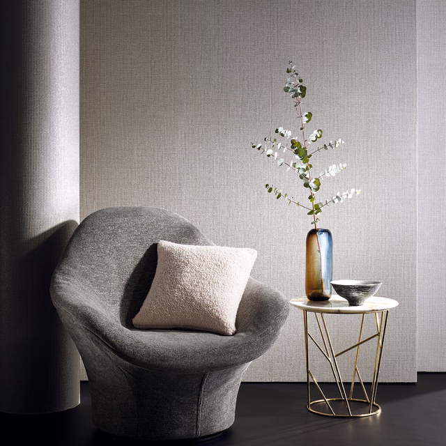 Soft grey textured wallpaper with fine vertical lines behind a charcoal sculptural chair