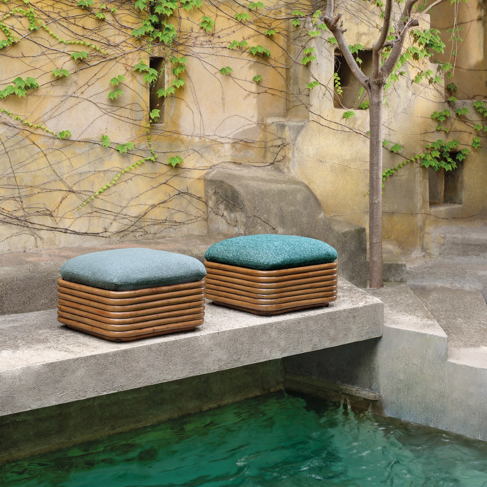 Cool teal textured cushions on rounded outdoor stools beside green-blue water