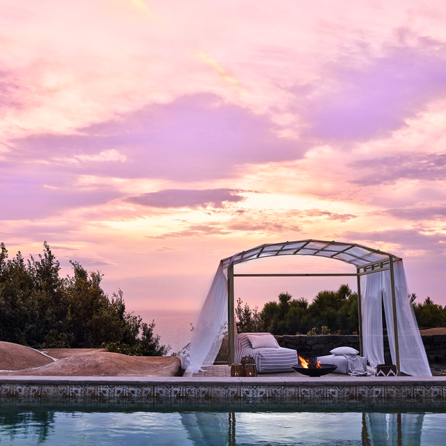 Chalky blush-pink outdoor upholstery on a poolside daybed at sunset