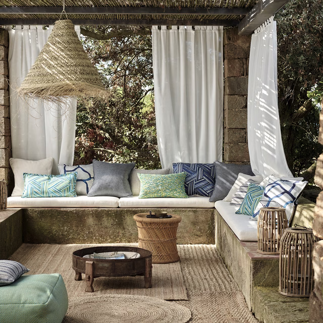 Muted ocean-blue and green patterned cushion fabric in a sunlit outdoor seating area