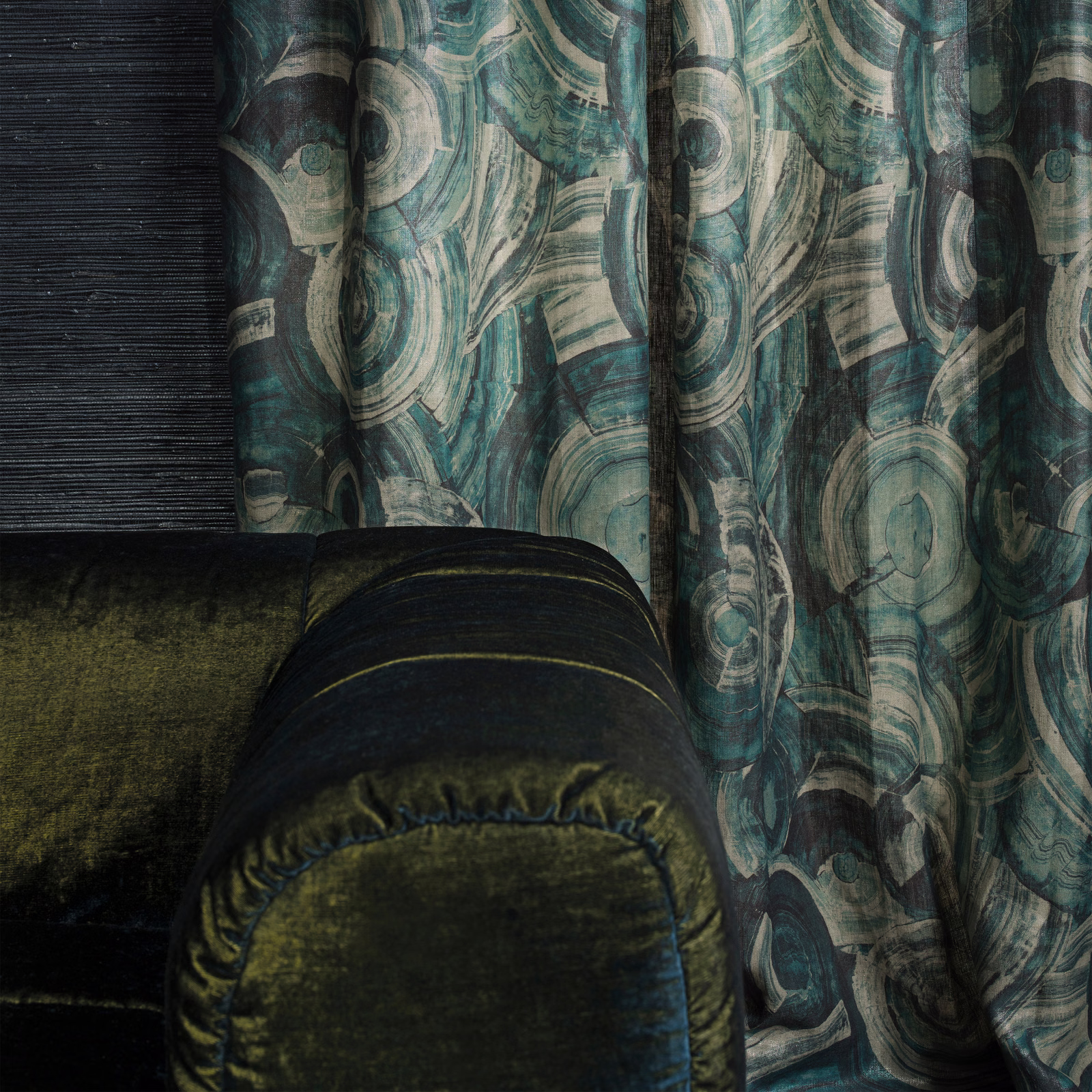 Deep teal abstract swirl fabric falling in folds beside dark olive seating