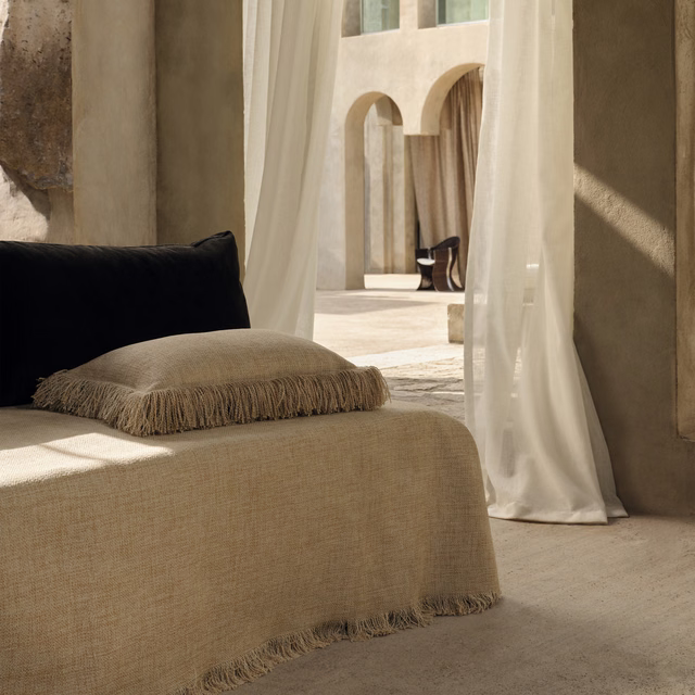 Warm coir-beige woven upholstery with fine texture on a fringed cushion