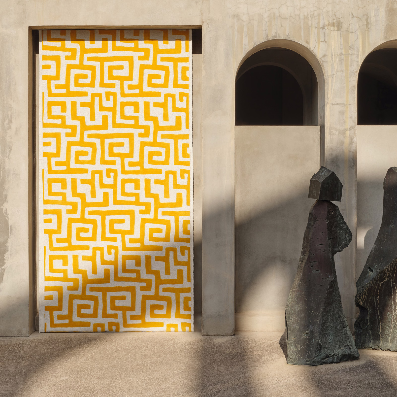 Ochre maze-pattern textile on an ivory ground in a sunlit architectural doorway