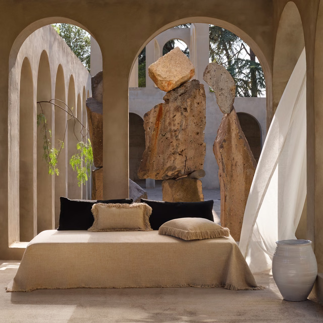 Warm sandy beige woven fabric draped across a bed with a softly frayed edge