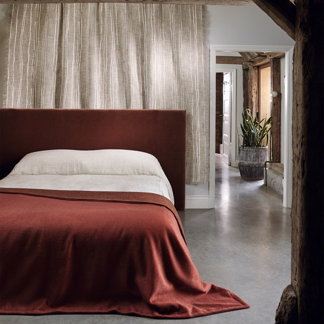 Deep spiced terracotta textile falling in softly lustrous folds across a bed